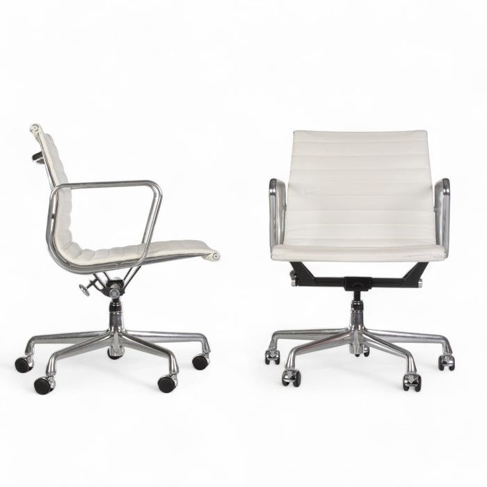 View of pair of white Eames EA335 office chairs, one from right side, one from front