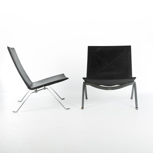View of pair of black leather Kjaerholm PK22 lounge chairs, one from right side, one from front