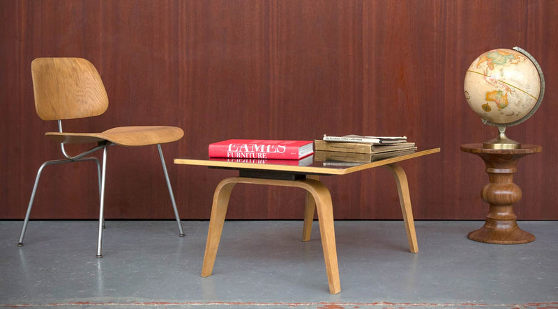 An original Eames DCM plywood dining chair sits alongside the OTW oblong shaped coffee tables and Ray Eames Walnut Stool and globe with wood paneling